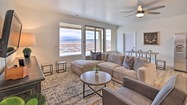 A modern living room with a sectional sofa, a coffee table, a TV, and a large window offering a view of the mountains. - Modern Apartment w/ Beautiful Mountain Views! (St. George)