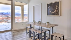A modern dining area with a large table and benches, a door, and a framed artwork on the wall. - Modern Apartment w/ Beautiful Mountain Views! (St. George)