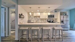 A modern kitchen with a central island, bar stools, a microwave, and a refrigerator.