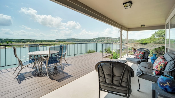 Ein Balkon mit Tisch und Stühlen, eine Couch mit Kissen und Blick auf einen See und Hügel.