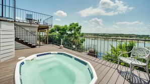 Eine Holzterrasse mit Whirlpool, einer weißen Bank und Blick auf einen Fluss und Bäume.