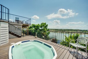 Una terraza de madera con un jacuzzi, un banco blanco y vistas a un río y árboles.