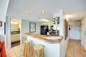 Una cocina con una isla central, taburetes de madera, un refrigerador y una alacena para vinos.