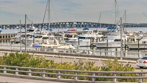 A marina with multiple boats docked, a bridge in the background, and a road with a guardrail in the foreground. - Walk to Beach From Chic Old Town Apartment w/ Yard (Bay St Louis)