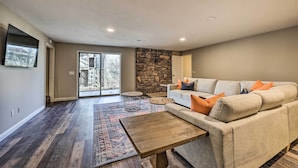 A spacious living room with a stone fireplace, a large sofa with orange cushions, and a wooden coffee table. - Spacious Bella Vista Home ~ 5 Mi to Lake! (Bella Vista)