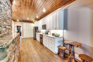 A kitchen with white cabinets, a stone wall, wooden flooring, and a wooden ceiling. - Hot Tub, Dock, Lakefront: Luxe Six Mile Retreat (Six Mile)