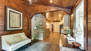 Un intérieur en bois avec une cheminée en pierre, un canapé blanc et un coin cuisine.