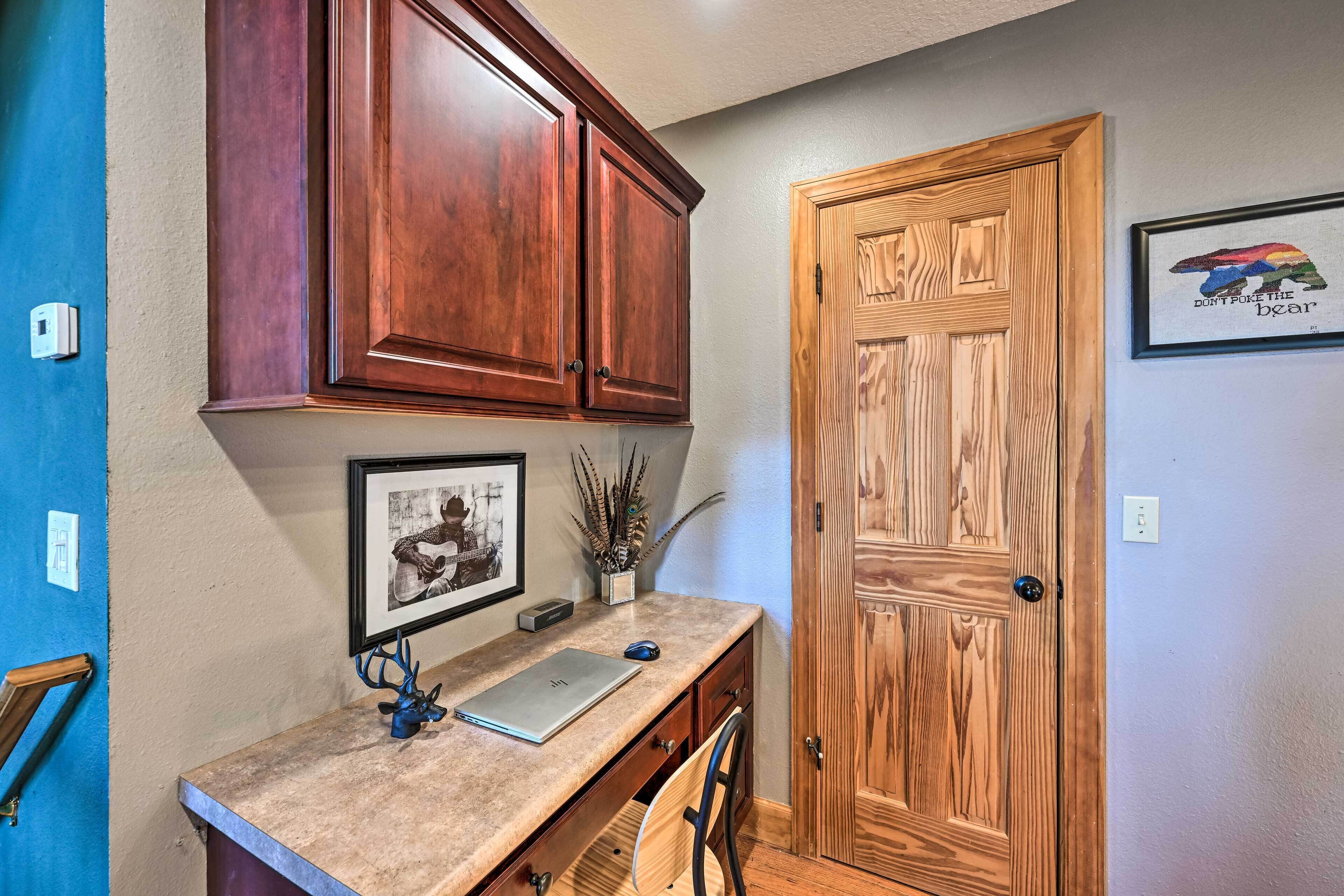 A home office with wooden cabinets, a desk with a laptop, a framed picture, and a door with a bear design.