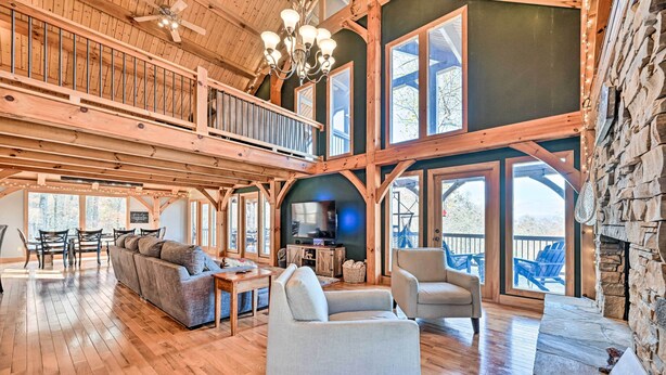 A spacious living area with a wooden floor, a large sofa, a fireplace, and a balcony with outdoor seating.