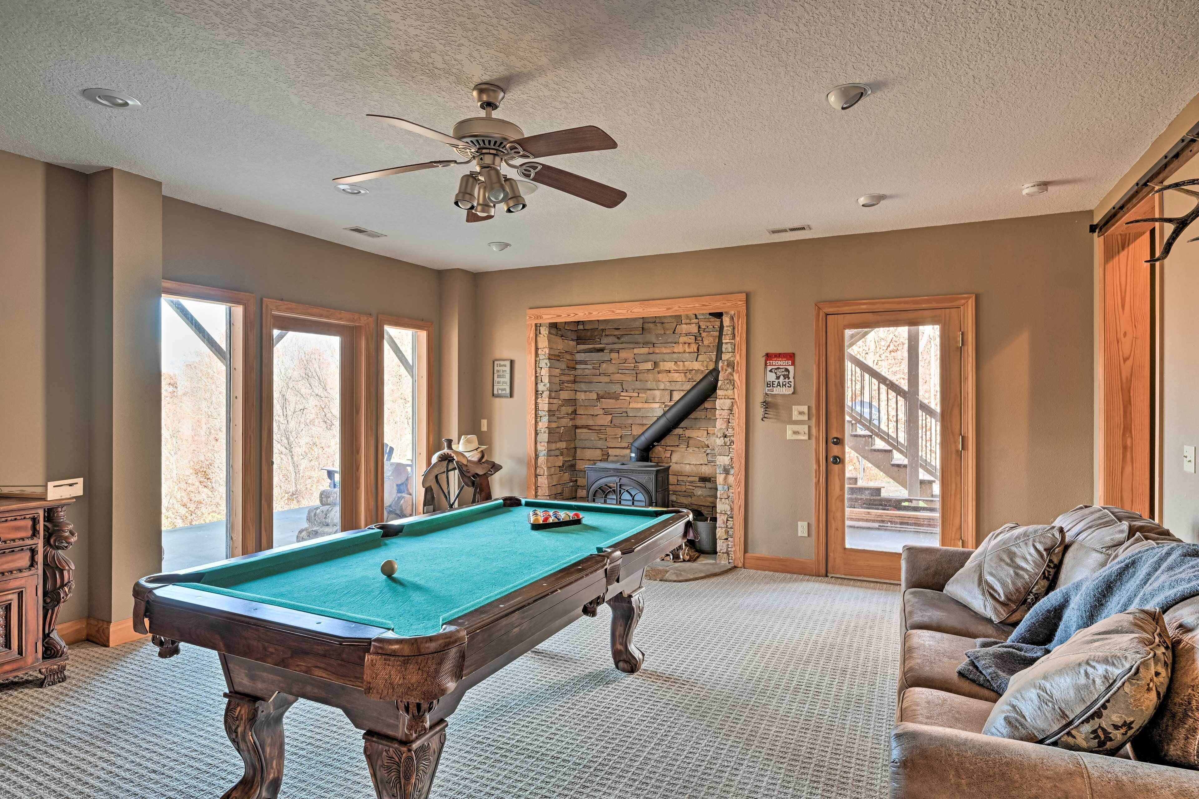 A pool table in a room with a stone fireplace, a couch, and a ceiling fan.