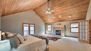 A spacious bedroom with a high ceiling, a fireplace, a large bed, and a view of the outdoors.