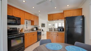 A kitchen with wooden cabinets, a black refrigerator, a microwave, and a stove. There is a dining table with blue placemats. - 2 Mi to Bonita Beach: Bbq-ready Townhome! (Bonita Springs)