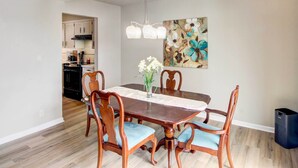A dining area with a wooden table, six chairs, a vase with flowers, and a painting on the wall. - Pleasant Condo - 14 Mi to Dtwn Kansas City (Overland Park)