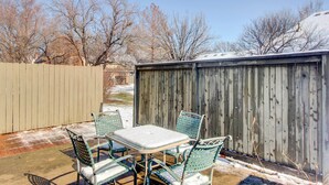 A patio with a table and chairs, a wooden fence, and leafless trees in the background. - Pleasant Condo - 14 Mi to Dtwn Kansas City (Overland Park)