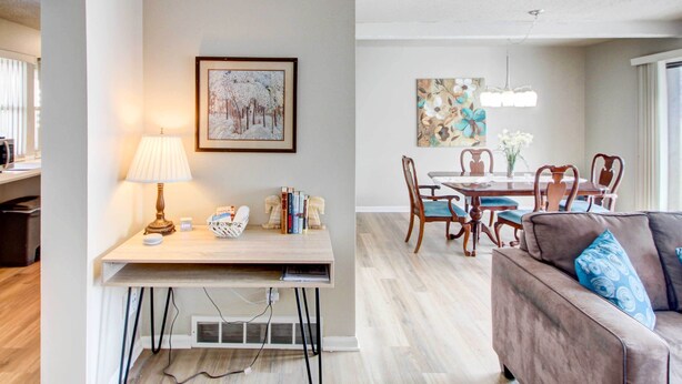 A modern living room with a wooden desk, a sofa, and a dining area with a table and chairs. - Pleasant Condo - 14 Mi to Dtwn Kansas City (Overland Park)