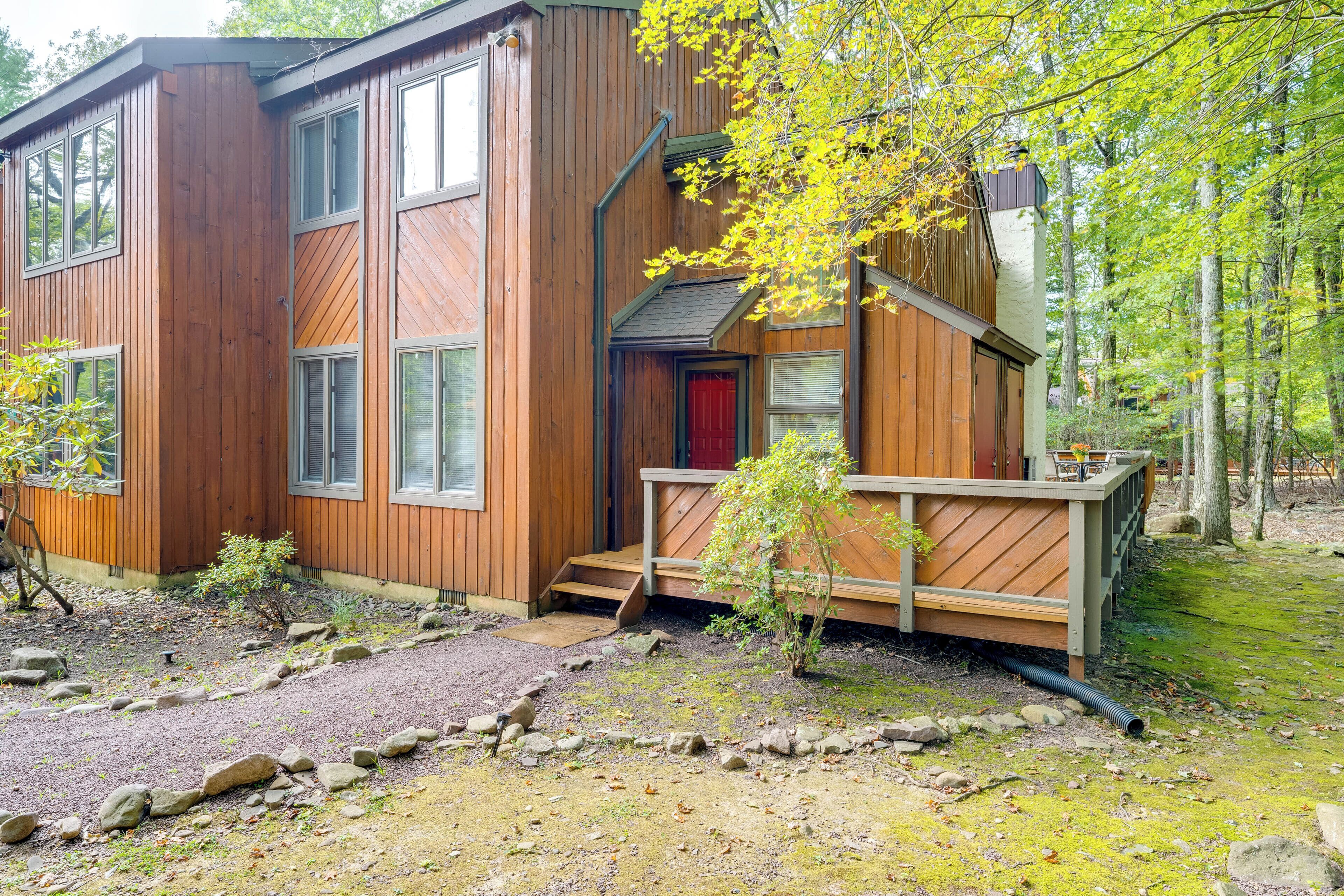 Une cabane en bois moderne dotée d’une terrasse, de grandes fenêtres et d’une porte rouge.