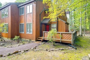 Una cabaña moderna de madera con terraza, ventanas amplias y puerta roja.