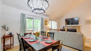 A dining area with a wooden table set for four, a chandelier, and a television mounted above a fireplace. - Near Skiing & Lakes: Contemporary Poconos Townhome (Lake Harmony)