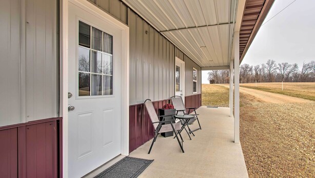 A covered porch with a white door, two folding chairs, and a concrete walkway. - Peaceful Missouri Cabin Rental on 55 Acres! (Canton)