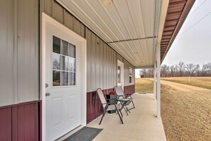 A covered porch with a white door, two folding chairs, and a concrete walkway. - Peaceful Missouri Cabin Rental on 55 Acres! (Canton)