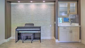 A room with a piano, a bench, a sink with a mirror, and a cabinet with glassware. - Palm Desert Retreat w/ Private Pool, Near Golf! (Palm Desert)