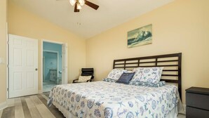 Un dormitorio con cama, mesita de noche, ventilador de techo y puerta que da a un baño.