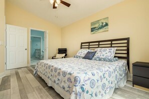Un dormitorio con cama, mesita de noche, ventilador de techo y puerta que da a un baño.