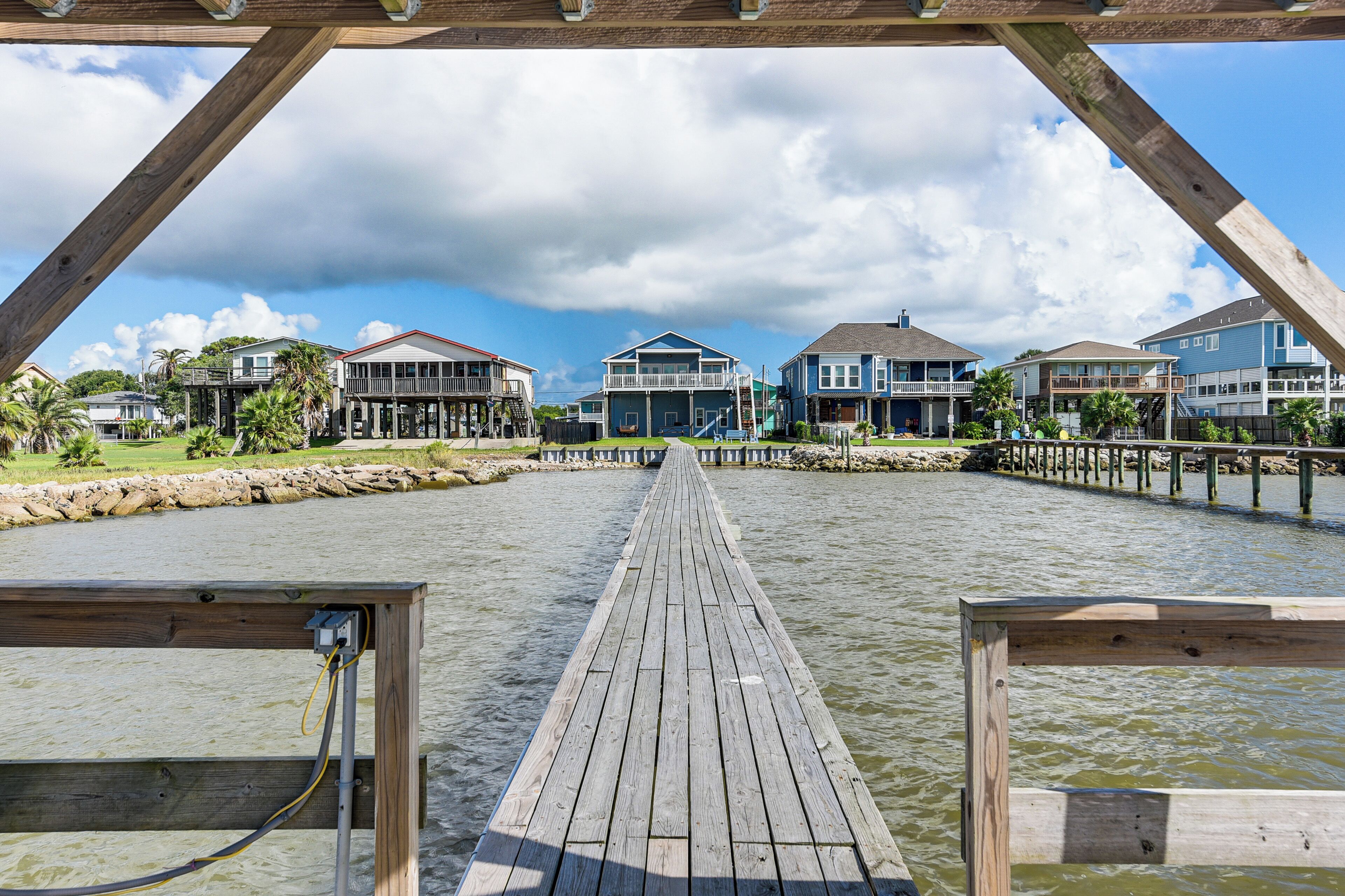 A wooden pier leading to a waterfront property with multiple houses and a clear sky.