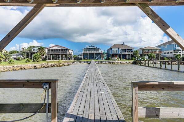 A wooden pier leading to a waterfront property with multiple houses and a clear sky. - On Galveston Bay: Spacious Home w/ Pier & Grills! (Dickinson)