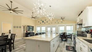 Una cocina amplia con una isla grande, muebles blancos y luminarias modernas.