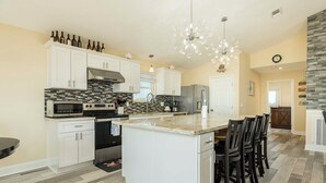 Una cocina amplia con armarios blancos, una isla grande y una lámpara moderna.
