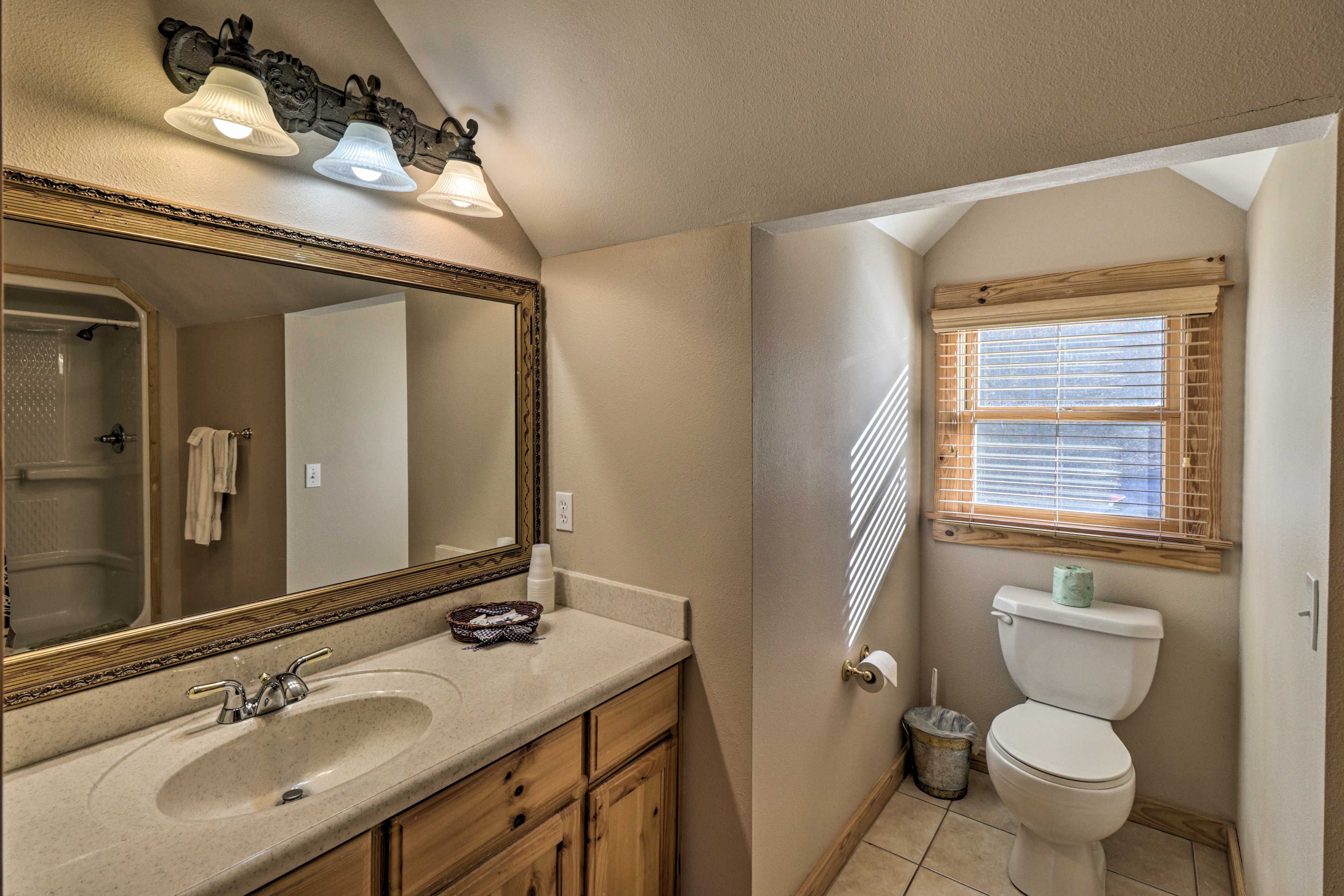 Une salle de bain avec un grand miroir, un lavabo, des meubles en bois, des toilettes et une fenêtre avec des stores.