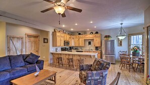 A spacious living area with a wooden floor, a sofa, a coffee table, and a dining area with wooden chairs and a chandelier. - Beaver Lake Retreat w/ Game Room & Spacious Deck (Rogers)