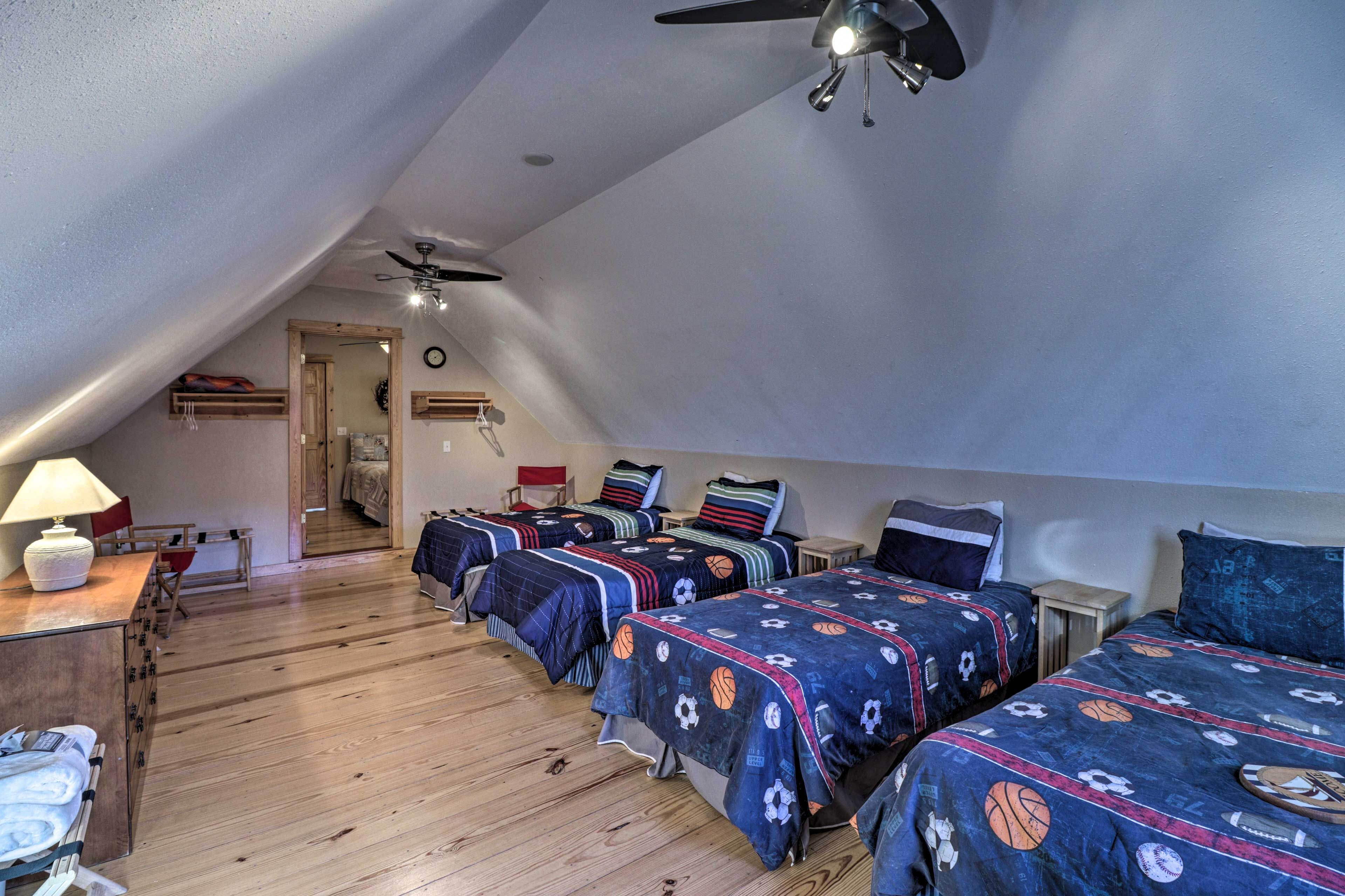 A room with four beds, wooden flooring, ceiling fans, and a desk with a lamp.