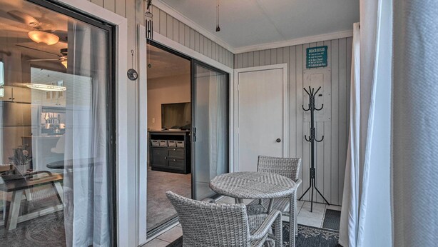 Una habitación con puerta corrediza de vidrio que da a una cocina, ventilador de techo, mesa con sillas y perchero.