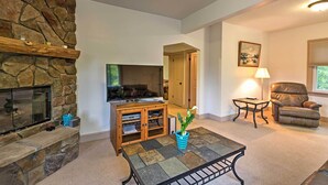 A living room with a stone fireplace, a flat-screen TV, a wooden entertainment unit, a blue basket, a potted plant, a leather recliner, and a lamp. - Hot Tub, Deck & Backyard: Cozy Union Pier House! (Union Pier)