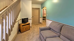 A hallway with a staircase, a wooden cabinet with a television, and a gray sofa. - Hot Tub, Deck & Backyard: Cozy Union Pier House! (Union Pier)