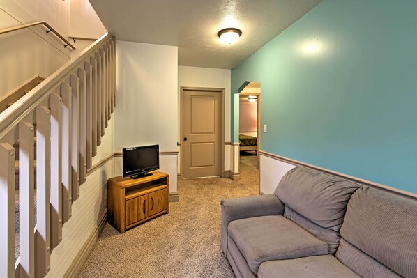 A hallway with a staircase, a wooden cabinet with a television, and a gray sofa.