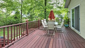 A wooden deck with a table and chairs, a red umbrella, and a potted plant. - Hot Tub, Deck & Backyard: Cozy Union Pier House! (Union Pier)