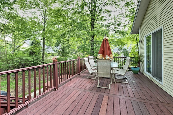 Um deck de madeira com mesa, cadeiras, um guarda-sol vermelho e um vaso de planta.
