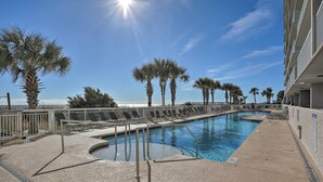 A pool area with palm trees, a clear sky, and a building with balconies.