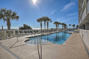A pool area with palm trees, a clear sky, and a building with balconies.