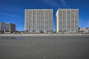 A beachfront hotel with multiple high-rise buildings, a sandy beach, and a clear blue sky.