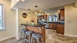 A kitchen with a bar area, wooden cabinets, and a marble floor. - Seaside Wildwood Haven: Walk to Boardwalk/beach! (Wildwood Crest)