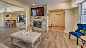 A spacious living room with a fireplace, a television mounted on the wall, and a dining area with a blue upholstered chair. - Seaside Wildwood Haven: Walk to Boardwalk/beach! (Wildwood Crest)