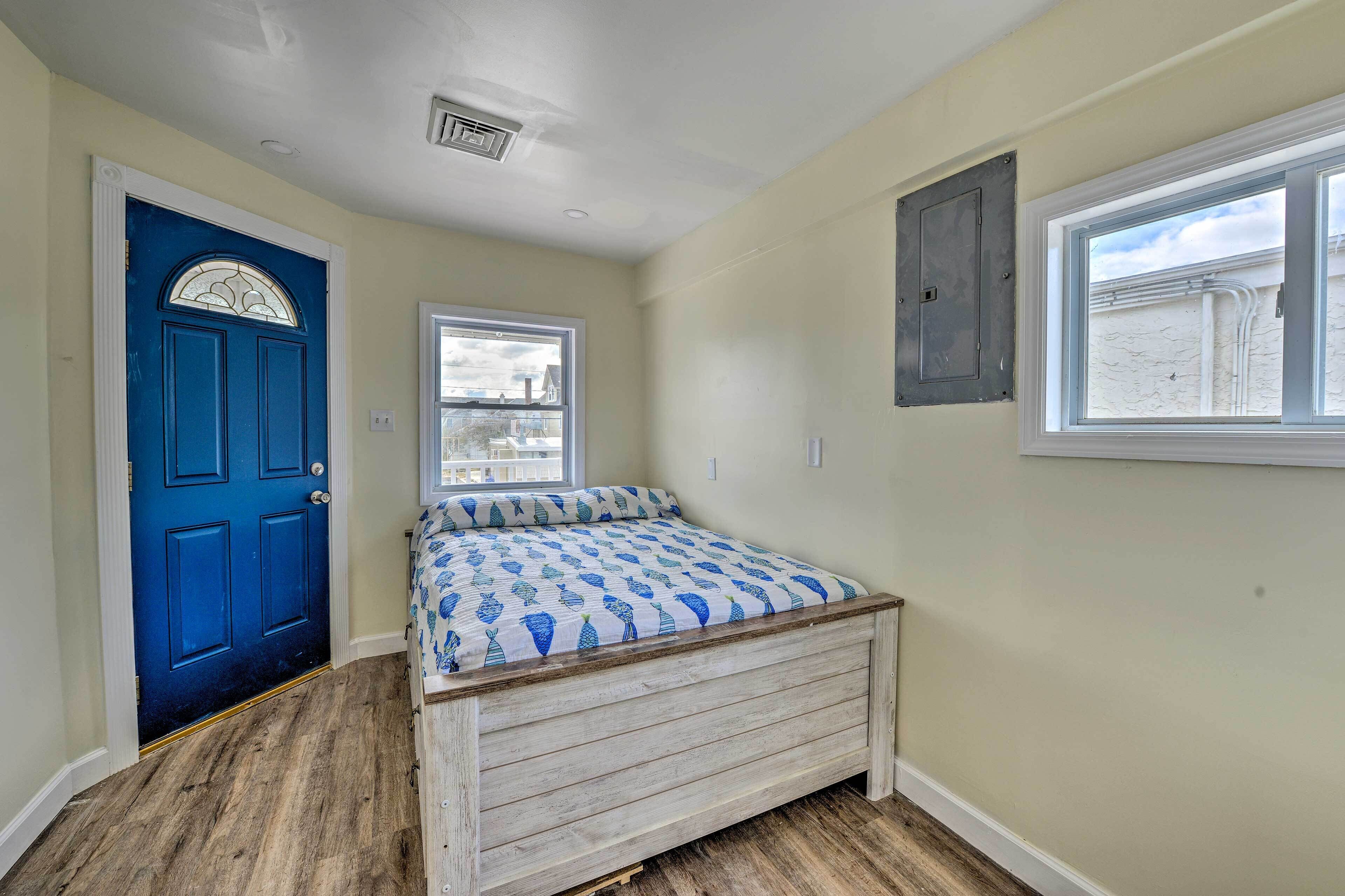 A bedroom with a blue door, a window, and a bed with a patterned bedspread.