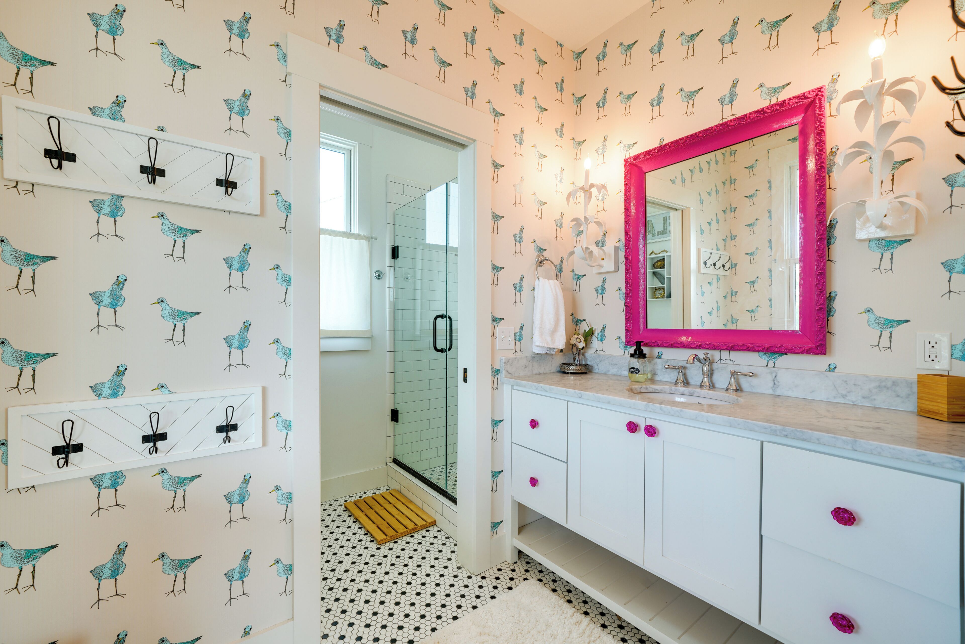 A bathroom with a white vanity, a pink-framed mirror, and a bird-patterned wallpaper.