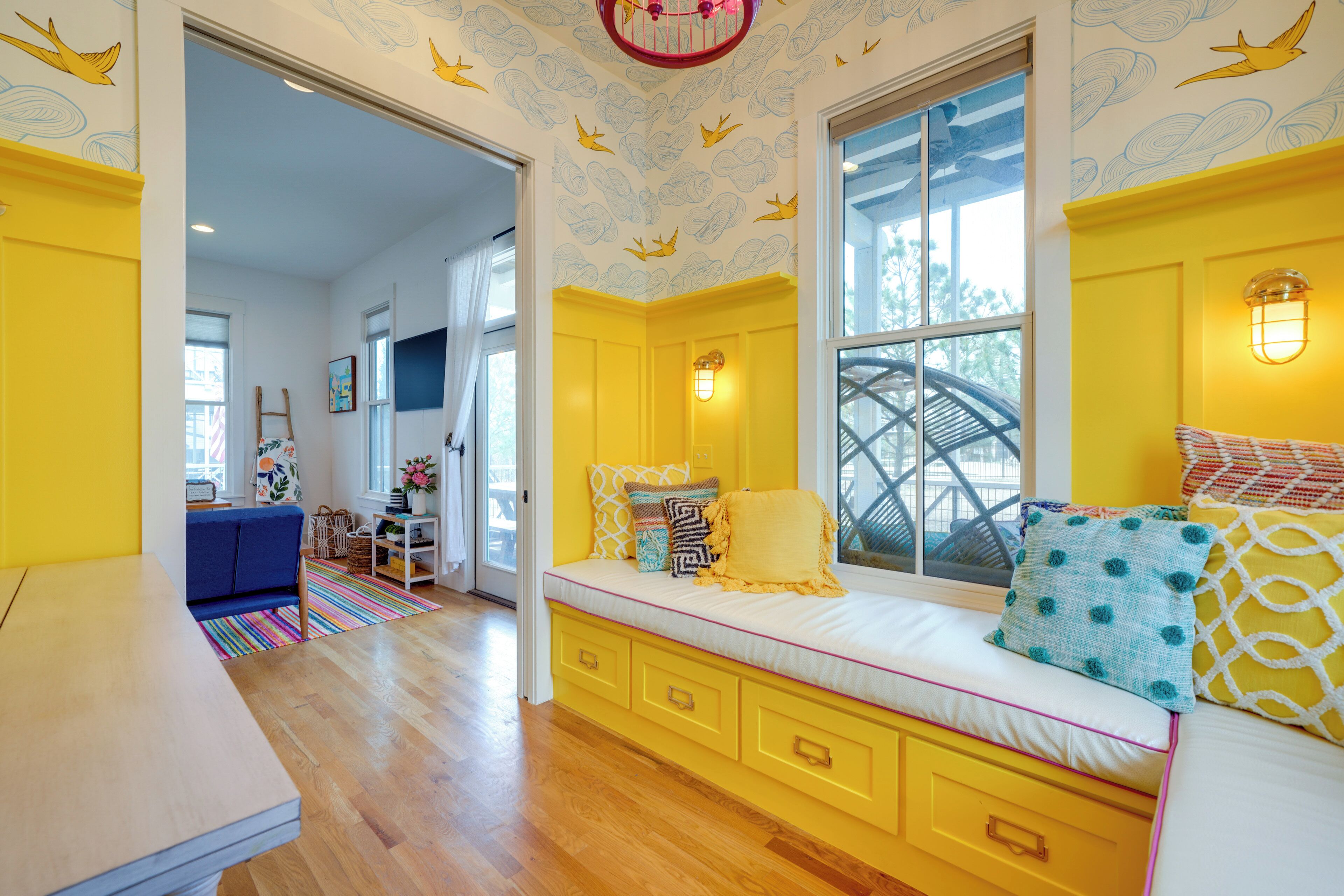 A bright yellow room with a large window, a built-in bench with cushions, and a view of the outdoors.