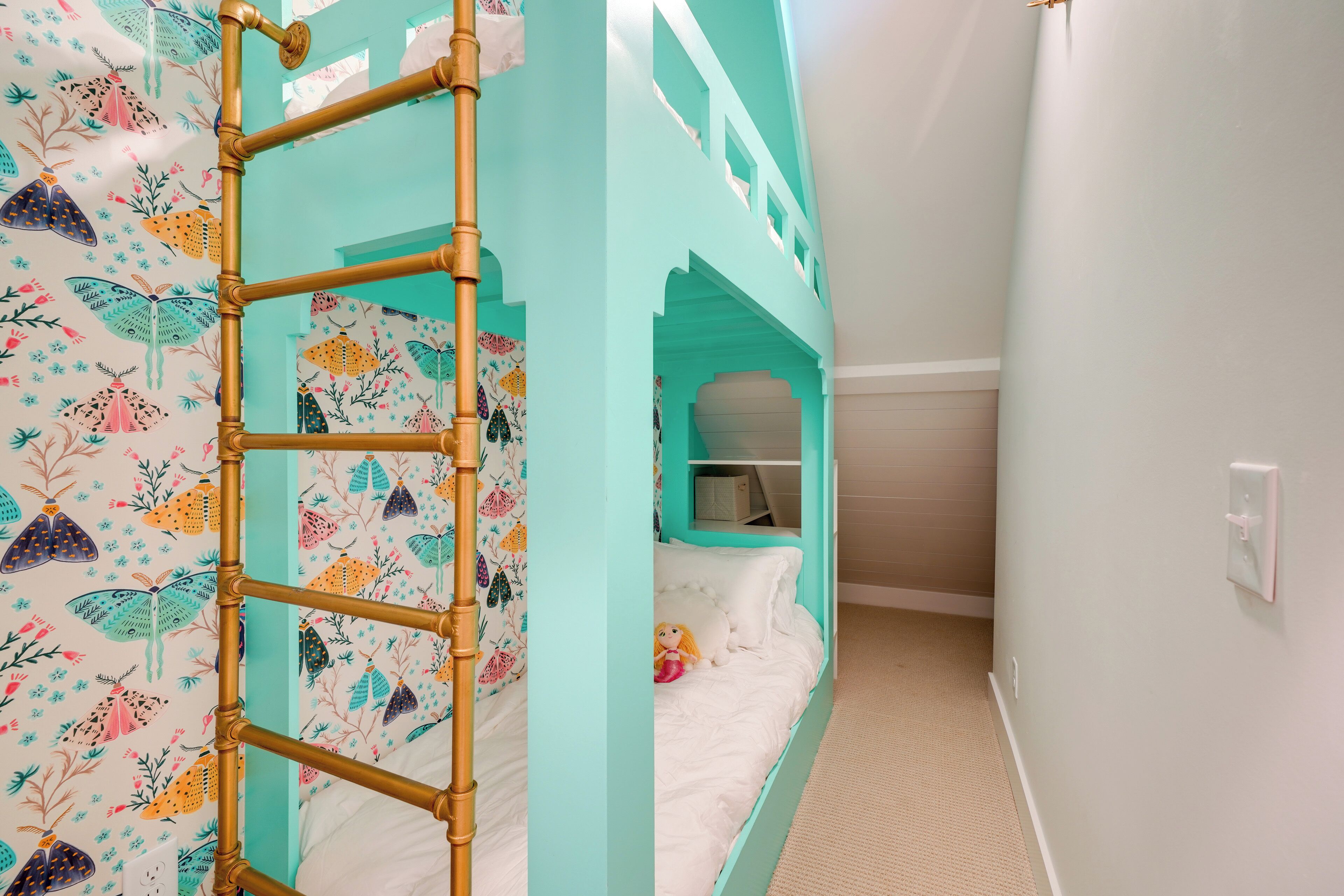 A bunk bed with a ladder, a small enclosed space with a desk, and a wall with a butterfly pattern.