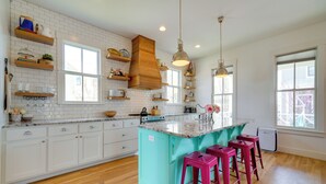 A kitchen with white cabinets, a turquoise island, wooden shelves, and pink bar stools. - Carlton Landing Home w/ Poolside Lake View! (Eufaula)